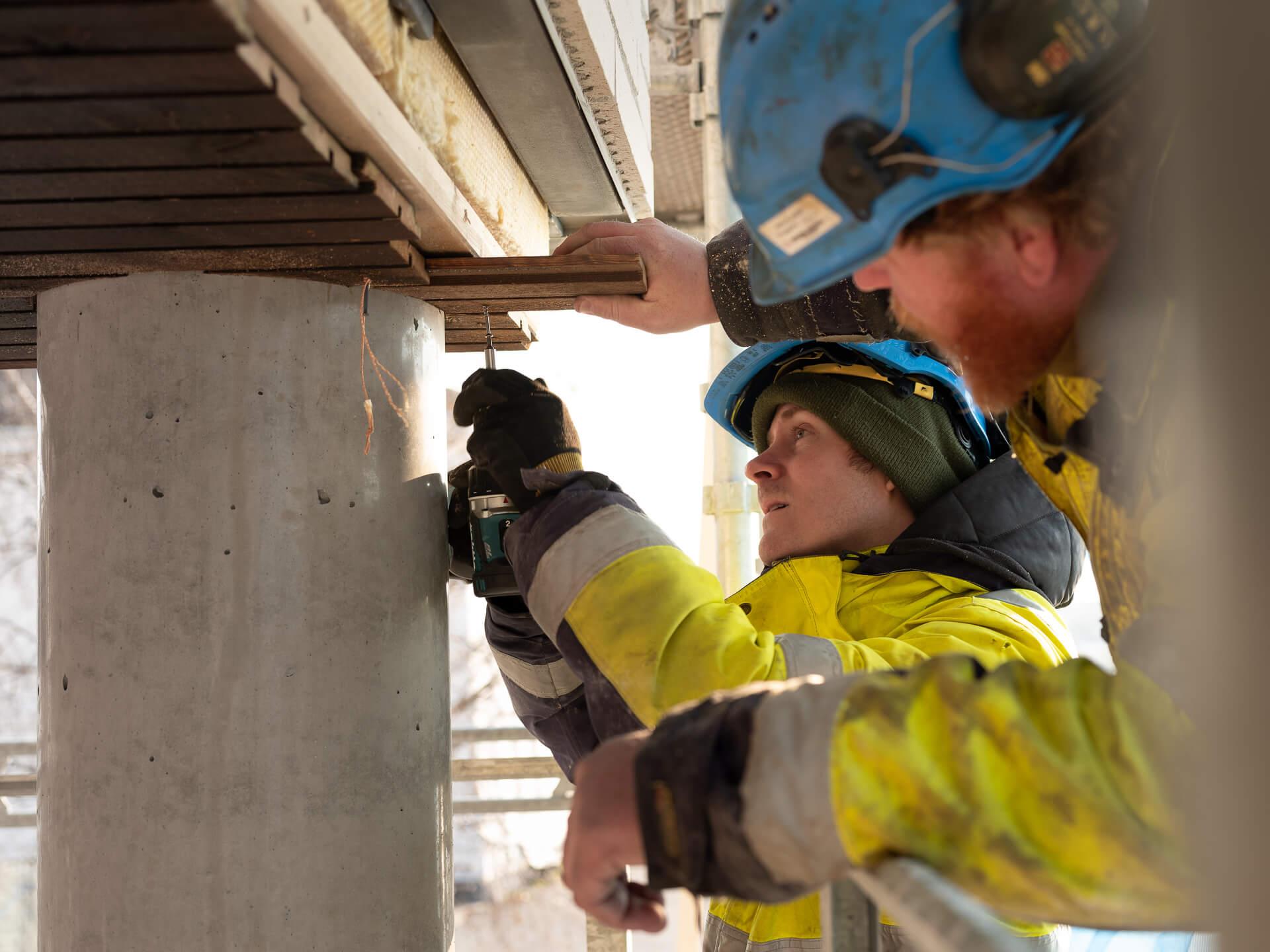 Two workers in hi-vis and helmets drilling into a concrete column
