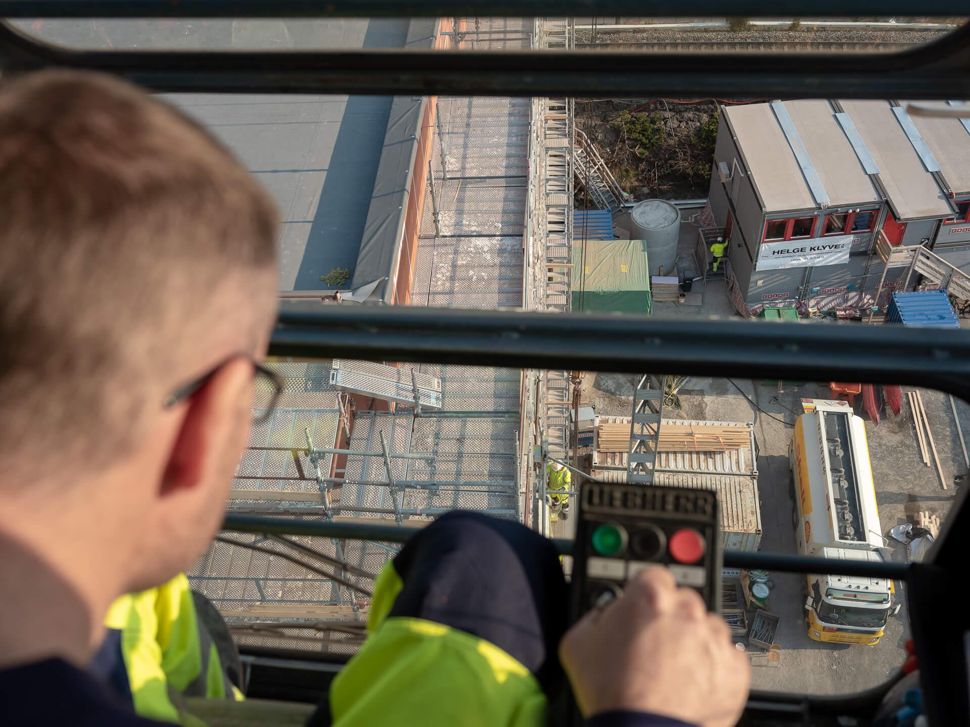 A crane operator at the controls in his cab, high above a building site