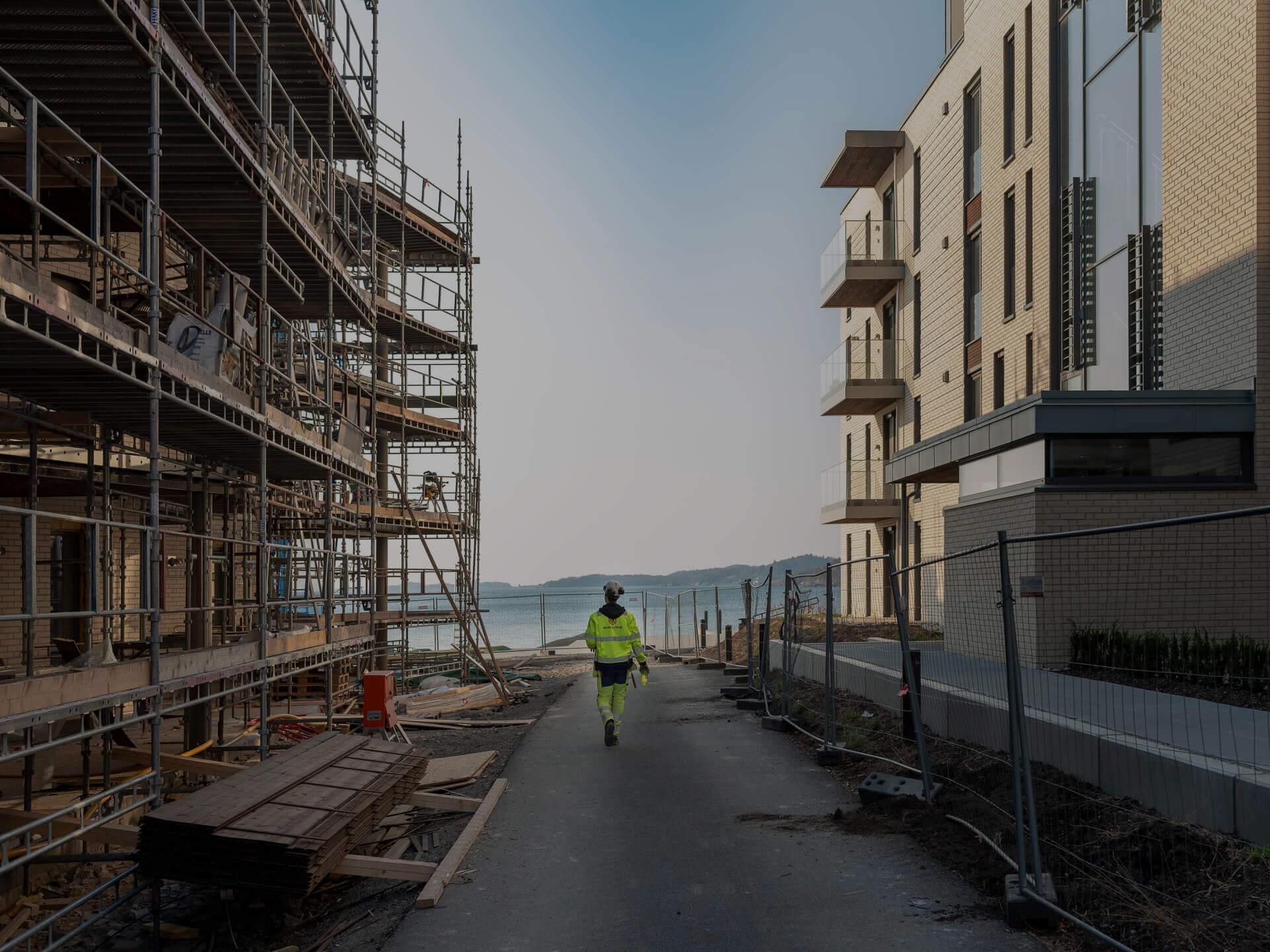 Scaffolding along a new apartment block by the sea, a worker walking on the path below
